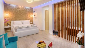 Een moderne slaapkamer met een bed, een rond bijzettafeltje met fruit, een blauwe bank en een houten scheidingswand.