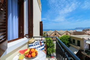 A balcony with a table of fruits and a straw hat, overlooking a coastal town with traditional buildings. - Diamond Suites (Chania)
