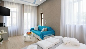 Een moderne hotelkamer met een blauwe bank, een glazen bijzettafeltje met fruit, een flatscreen televisie en een bed met handdoeken.