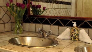 Un lavabo de salle de bain avec un robinet, un vase de tulipes violettes et un flacon de savon pour les mains.