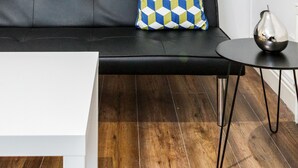Ein modernes Wohnzimmer mit einer schwarzen Couch, einem gemusterten Kissen, einem weißen Couchtisch und einem kleinen Beistelltisch mit einer Vase.