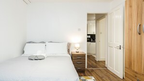 Ein Schlafzimmer mit einem Bett, einem Nachttisch mit Lampe, einem Holzschrank und einer Tür zu einer Küche.