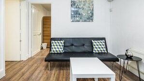Ein modernes Wohnzimmer mit einem schwarzen Ledersofa, zwei gemusterten Kissen, einem weißen Couchtisch und einem geometrischen Kunstwerk an der Wand.