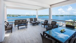 A covered outdoor seating area with a glass table, chairs, and a sofa, overlooking a body of water with boats and distant land. - Hamilton Princess - Fairmont Gold Experience (Pembroke Parish)