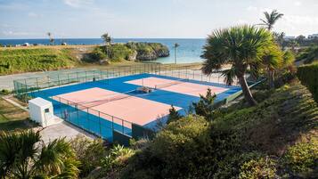 Una cancha de tenis con red, rodeada de vegetación y vista al océano.