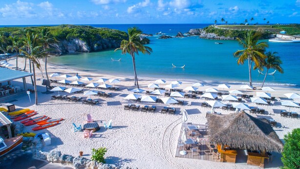 A beach resort with multiple lounge areas, umbrellas, and a thatched-roof hut. - Hamilton Princess - Fairmont Gold Experience (Pembroke Parish)