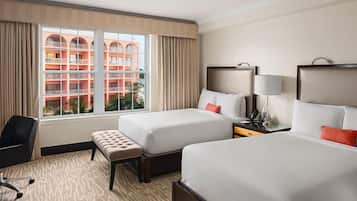 Habitación de hotel con dos camas, un escritorio, una silla y ventana con vista a un edificio.