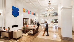 A spacious lobby with a high ceiling, marble flooring, and a chandelier. There are seating areas with sofas and a coffee table. A large blue sculpture and colorful artwork adorn the walls. - Hamilton Princess - Fairmont Gold Experience (Pembroke Parish)