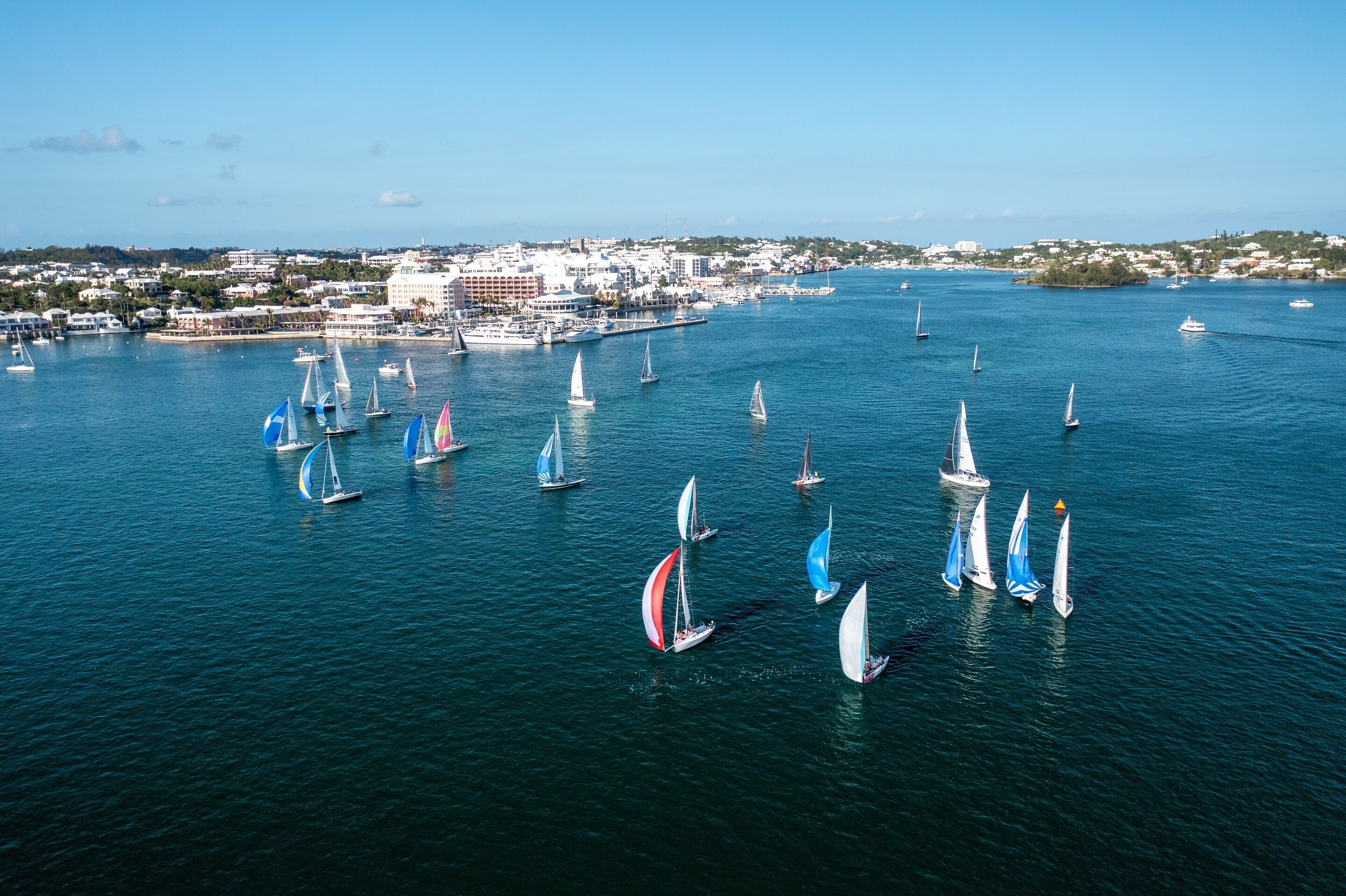 Un port de plaisance avec de nombreux voiliers, et une ville côtière en arrière-plan.