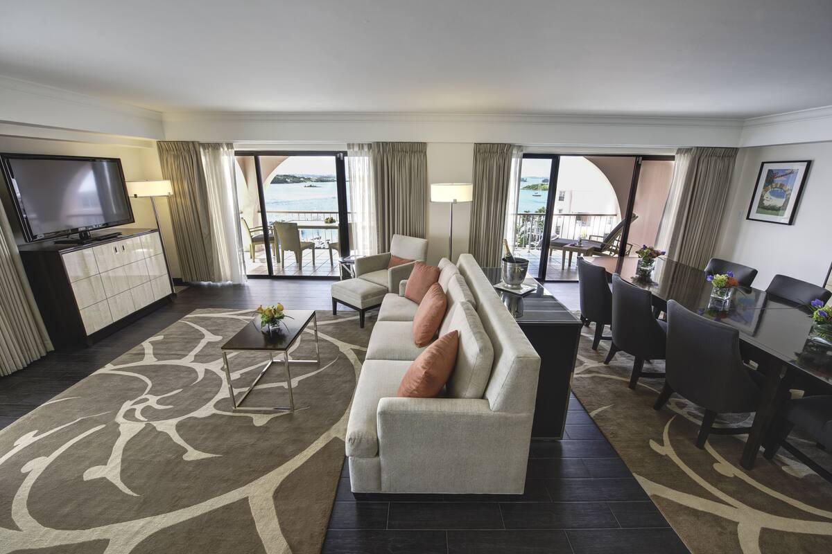Ein Hotelzimmer mit Sofa, Fernseher, Esstisch, Stühlen und Meerblick.