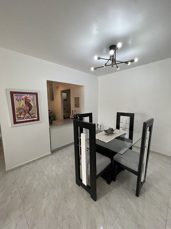 A dining area with a glass table, black chairs, a ceiling light fixture, and a framed artwork on the wall.