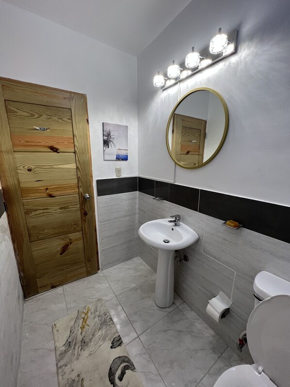 Un baño con puerta de madera, lavamanos blanco, espejo y retrete.