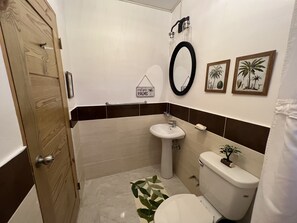 A bathroom with a wooden door, a white sink, a toilet, and two framed pictures on the wall. - Eclectic and comfortable apartment in El Paraiso Cabrera—2 minutes from downtown (Cabrera)