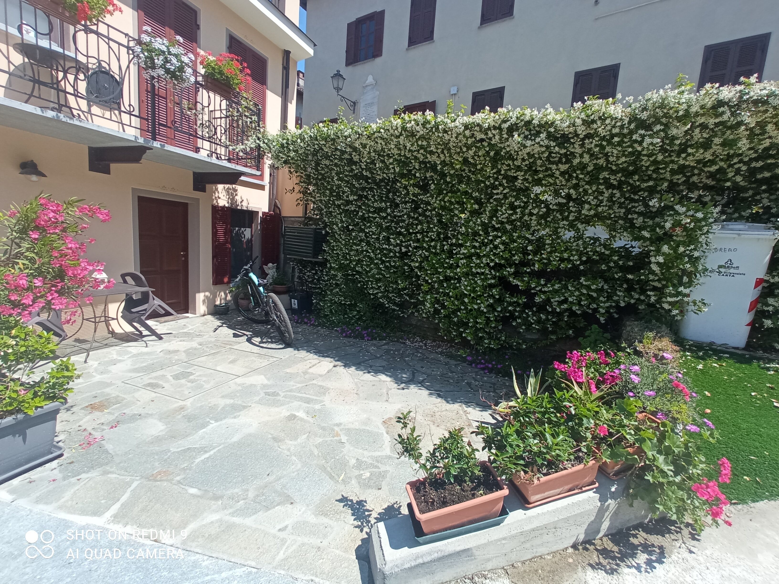 Un patio con suelo de piedra, una motocicleta, plantas en macetas y un seto.