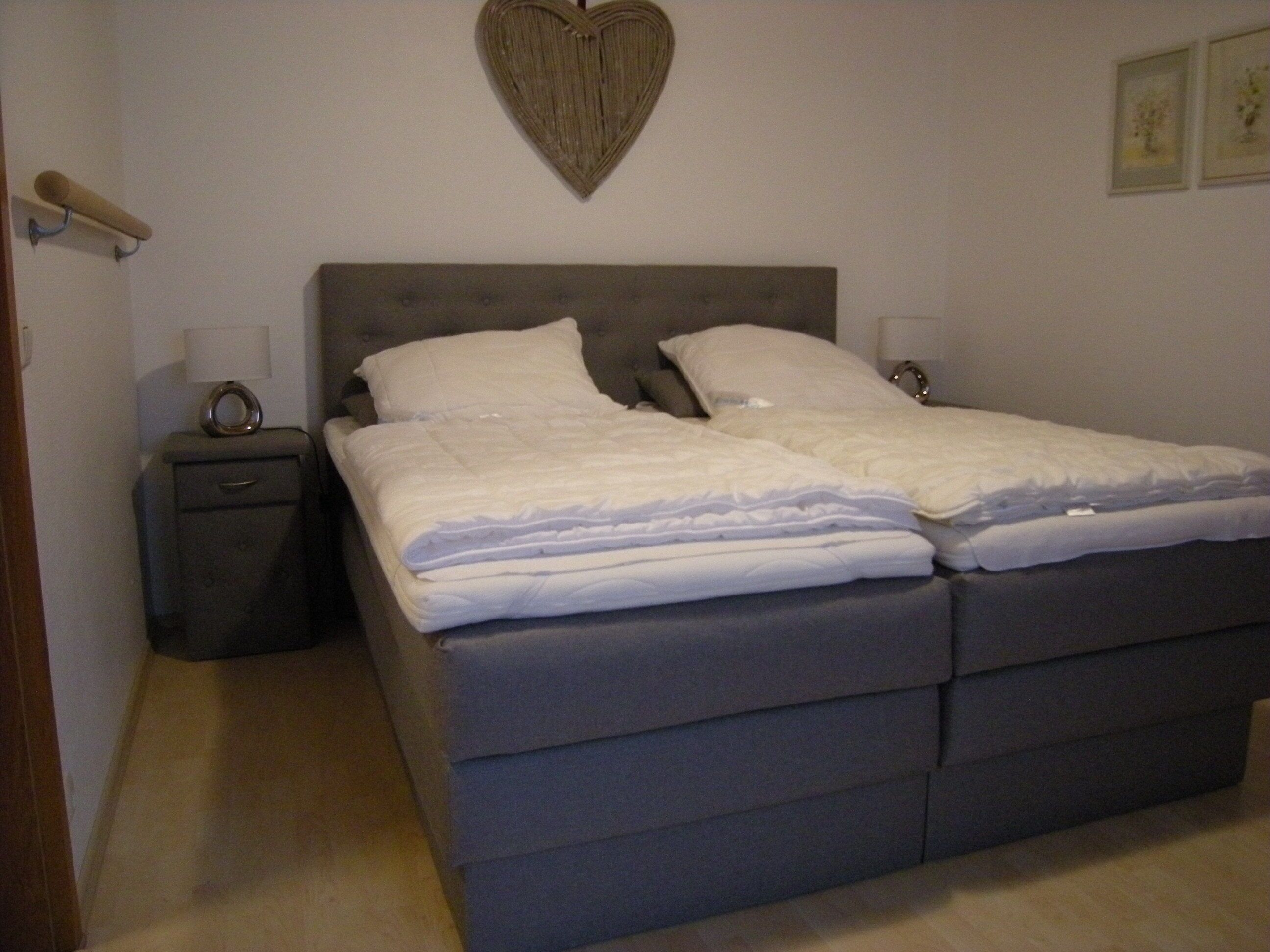 Ein Schlafzimmer mit einem Doppelbett, zwei Nachttischen, einer Wanddekoration in Herzform und einem kleinen Beistelltisch.