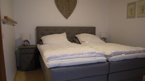 Een slaapkamer met een tweepersoonsbed, twee nachtkastjes, een hartdecoratie aan de muur en een klein nachtkastje.