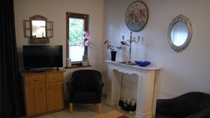 Een woonkamer met een televisie, een open haard, een klok en twee stoelen.