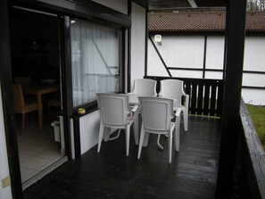 An outdoor patio with a table and chairs, a sliding glass door leading to an interior space, and a small outdoor light fixture. - Bungalow 31 on the edge of the forest with 1 bedroom. (Dipperz)