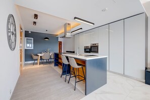 A modern kitchen with a central island, built-in appliances, and a dining area with a large clock.