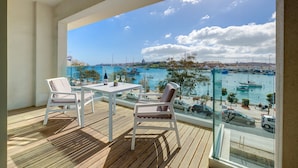 Een balkon met een tafel en stoelen, met uitzicht op een jachthaven vol boten en een stadsgezicht.