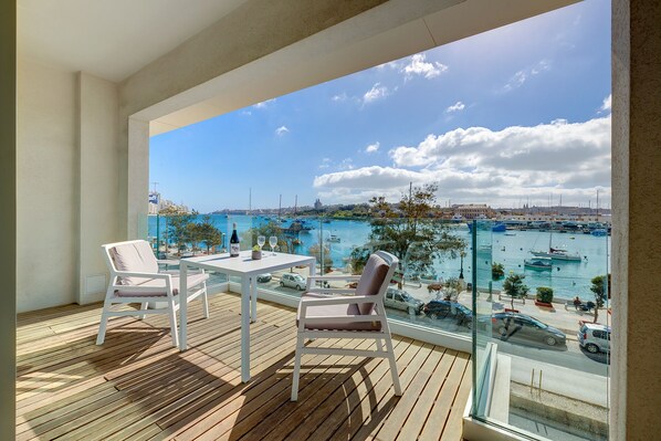 A balcony with a table and chairs, overlooking a marina with boats and a cityscape.