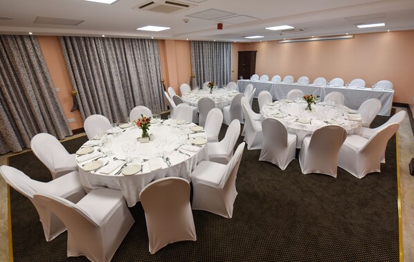 A conference room with round tables, white chairs, and a carpeted floor.