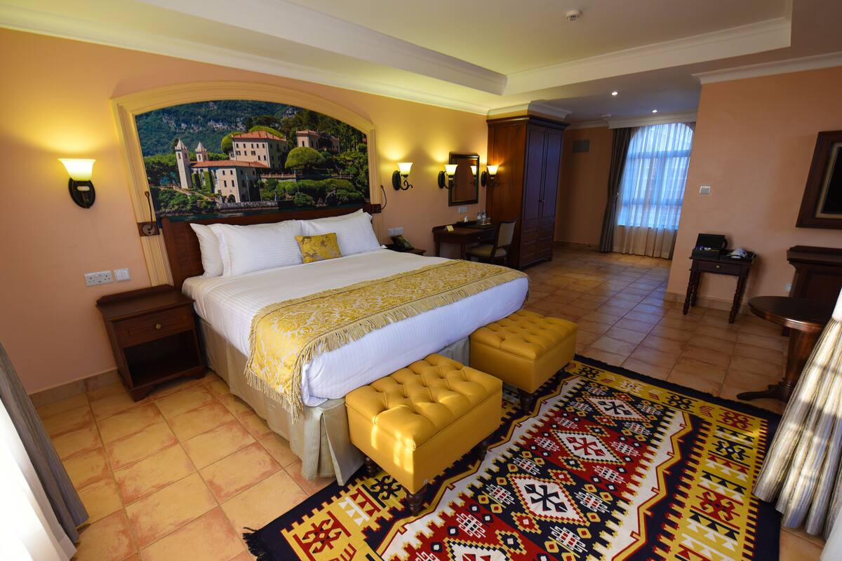 Habitación de hotel con una cama grande, un banco, un escritorio y un cuadro en la pared.