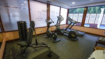 Une salle de sport équipée de divers appareils d’exercice, notamment un banc de développé couché, un vélo elliptique et un tapis de course.