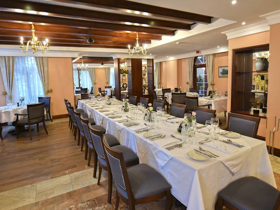 Une salle à manger avec de longues tables dressées pour le repas, un plancher en bois et des lustres.