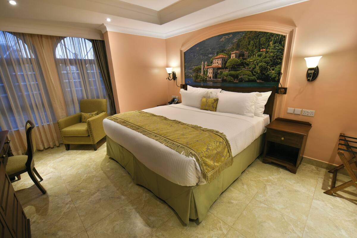 Habitación de hotel con una cama grande, una silla, una mesita de noche y un cuadro en la pared.