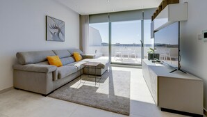 A modern living room with a grey sofa, a small coffee table, and a view of the sea through large glass doors. - Superlative Penthouse, Valletta and Harbour Views (Sliema)