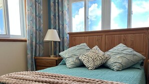 Une chambre à coucher avec un lit, une table de chevet, une lampe et une fenêtre avec des rideaux.