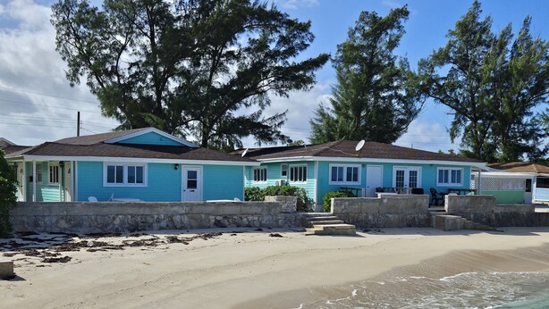 Une propriété située en bord de mer, comprenant deux maisons aux couleurs turquoise, une plage de sable et une vue dégagée sur l’océan.