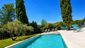 Ein rechteckiger Swimmingpool mit klarem, blauem Wasser, umgeben von einer Holzterrasse und einer gefliesten Liegefläche mit Liegestühlen.