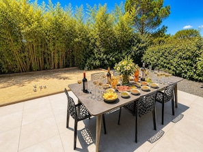 An outdoor dining area with a table set for a meal, surrounded by chairs, and a bottle of wine on the table. - La casa du Lez (Montferrier-sur-Lez)