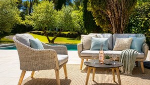 Eine Terrassenfläche mit Korbmöbeln, einem Pool und Blick auf einen gepflegten Garten.