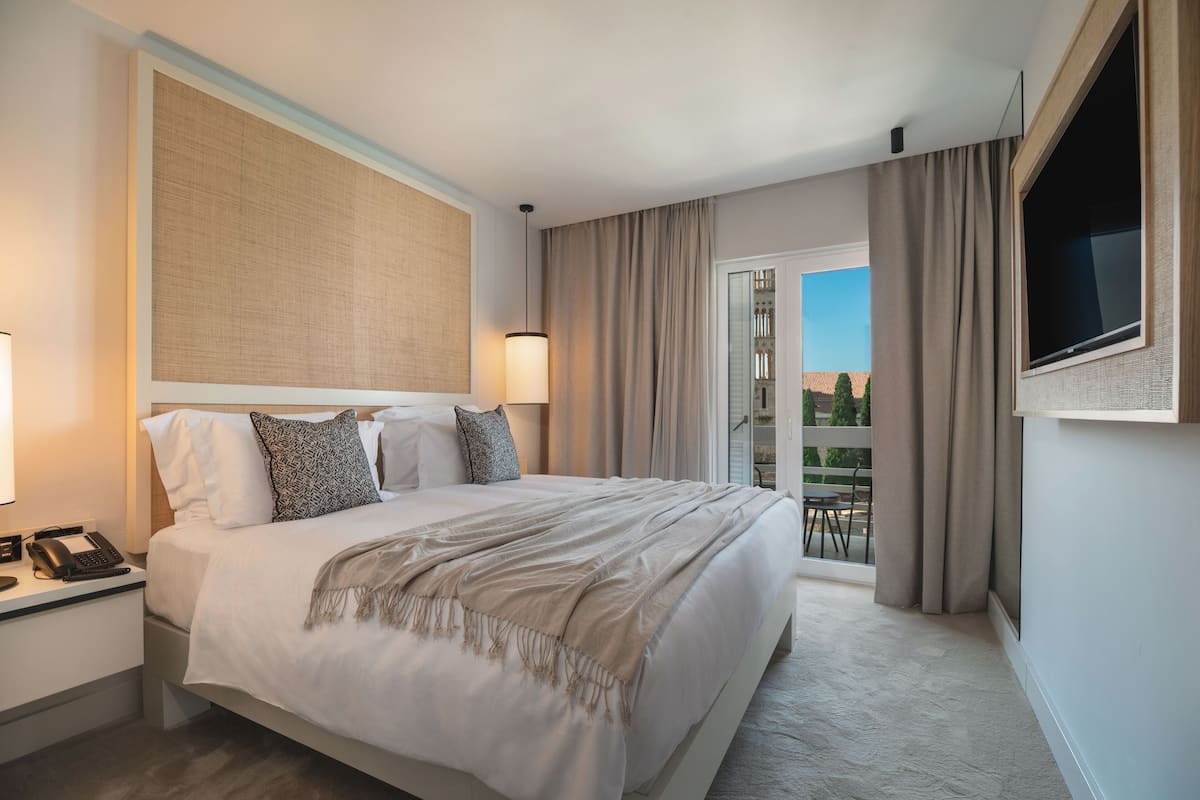 Quarto de hotel com uma cama grande, telefone ao lado da cama, televisão na parede e varanda com cortinas.