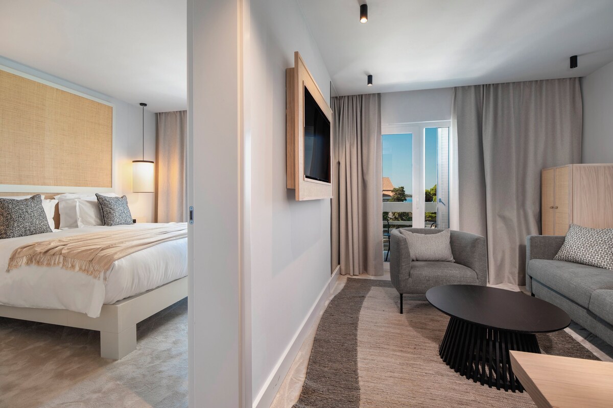 A modern hotel room with a bed, a sofa, a TV, and a balcony view.