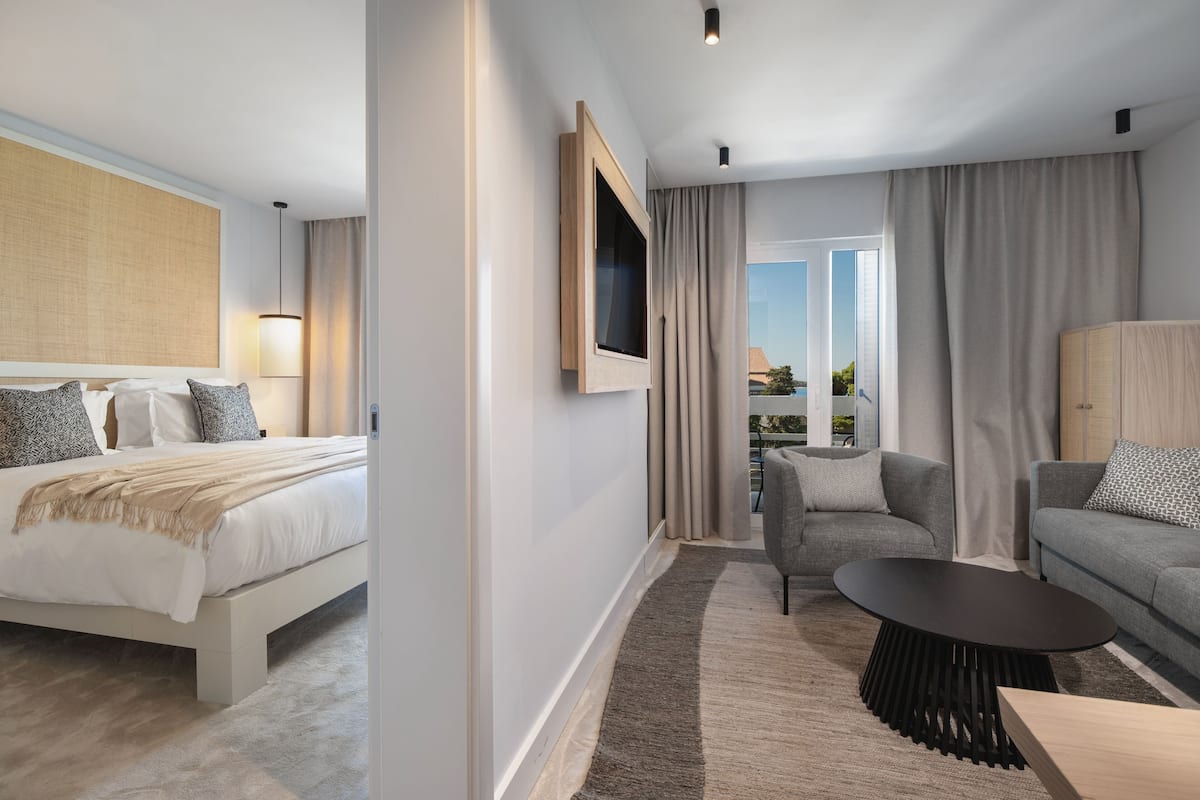 Quarto de hotel moderno com cama, sofá, televisão e vista para a varanda.