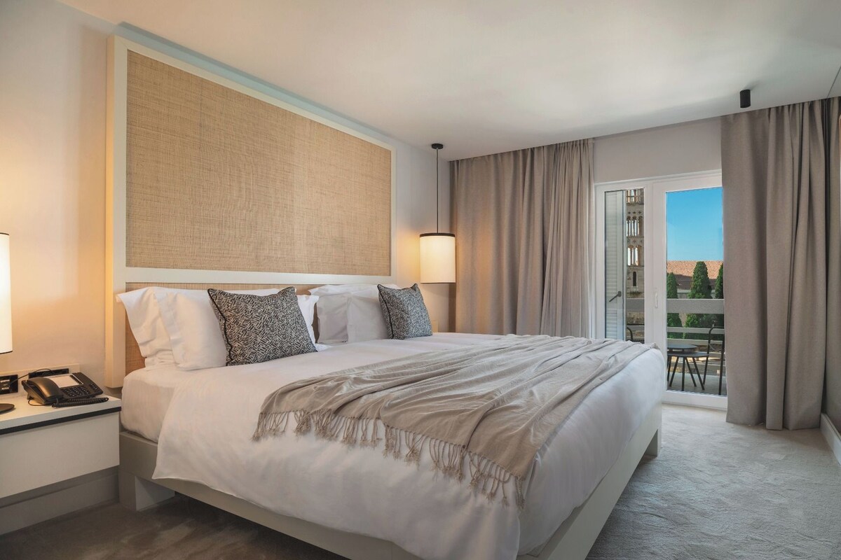 A hotel room with a bed, bedside table, lamp, and a TV mounted on the wall.