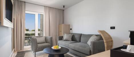Una sala de estar moderna con un sofá gris, una mesa de centro redonda negra con frutas, una silla de mimbre y un televisor montado en la pared.