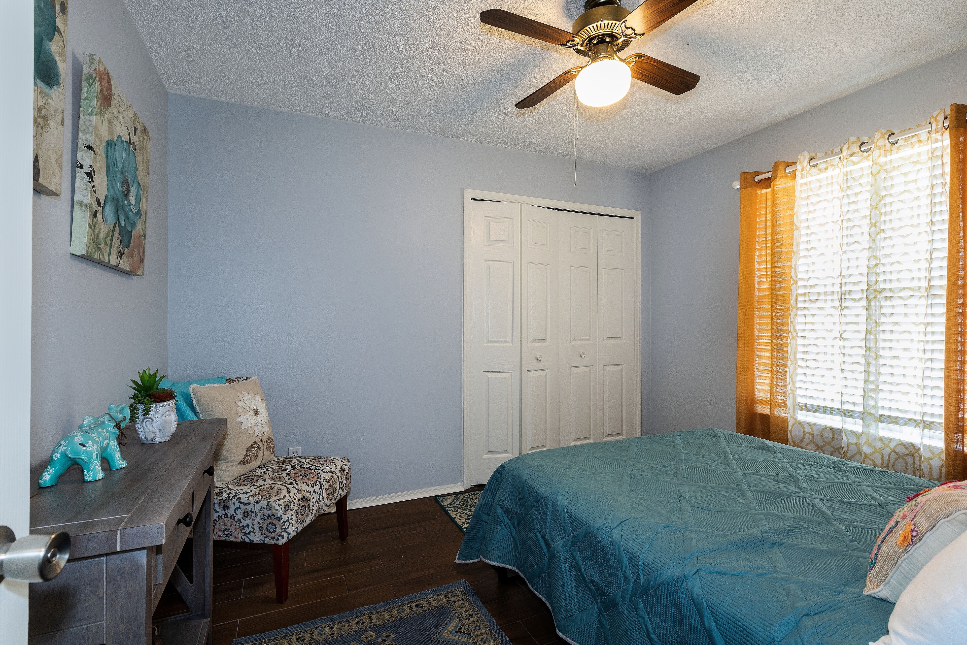 A bedroom with a bed, a desk, a chair, a ceiling fan, and a door.