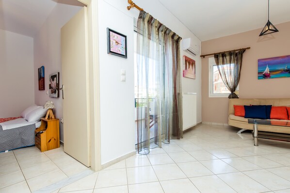 A room with a bed, a wooden nightstand, a sofa, and a window with curtains.