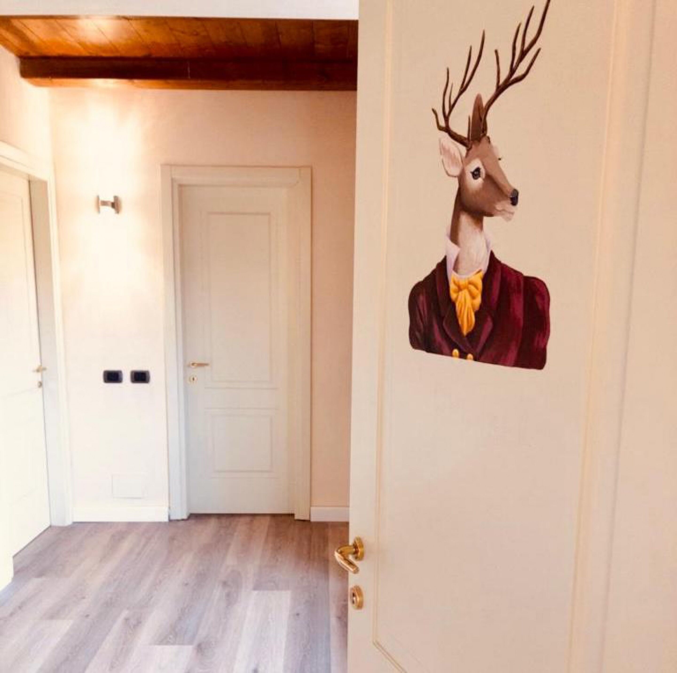 Un pasillo con una puerta blanca, techo de madera y un muro decorado con un ciervo.