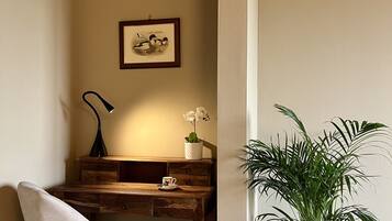 Ein Eckzimmer mit Holztisch, Stuhl, gerahmtem Bild an der Wand, Lampe, kleiner Topfpflanze und großer Topfpflanze.