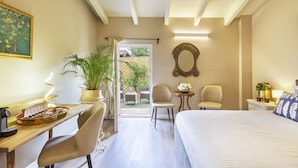 Habitación de hotel con cama, escritorio con objetos sobre una bandeja, una silla, una mesita con planta y vistas al exterior.