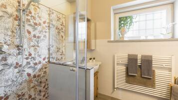 Een badkamer met een douche, wastafel, spiegel en raam.