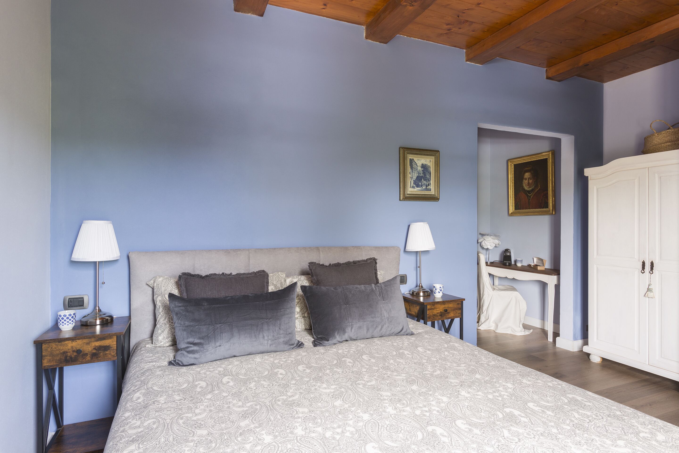 A bedroom with a large bed, two bedside tables with lamps, a wardrobe, and a desk with a chair.