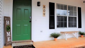 Une porte verte avec un paillasson, une enseigne en bois portant les mots « HOME » et « Sweet Home », et un panneau indiquant le numéro « 609 » sur une maison blanche.