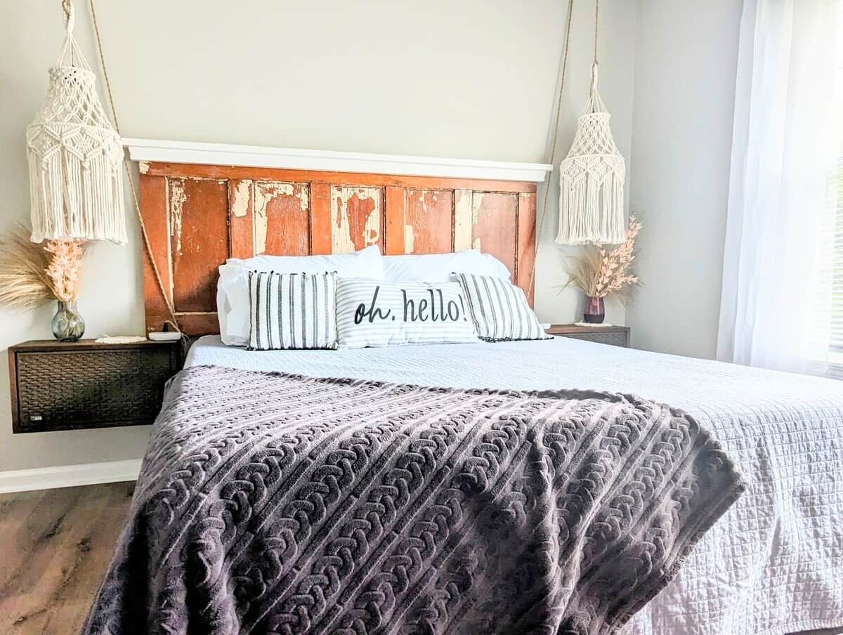 A bedroom with a wooden headboard, two macramé wall hangings, a bed with striped pillows, and a textured blanket.
